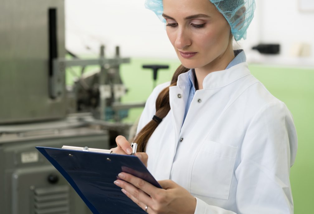 Portrait of a female inspector writing observations about equipment and manufacturing process during quality control in a cosmetics factory